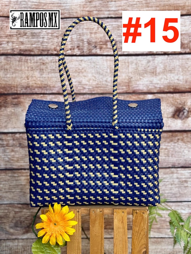 Op de afbeelding: Een rechthoekige gevlochten tas met een geometrisch patroon in donkerblauw en cr&egrave;me. De tas heeft twee gevlochten hengsels in bijpassende kleuren en twee zilverkleurige metalen drukknopen aan de bovenrand. De tekst #15 is zichtbaar.