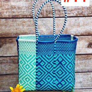 May include: A rectangular woven tote bag featuring a geometric diamond pattern in shades of light blue, turquoise, and dark blue. The bag has two braided handles in a matching blue and white color scheme and a structured open top design.