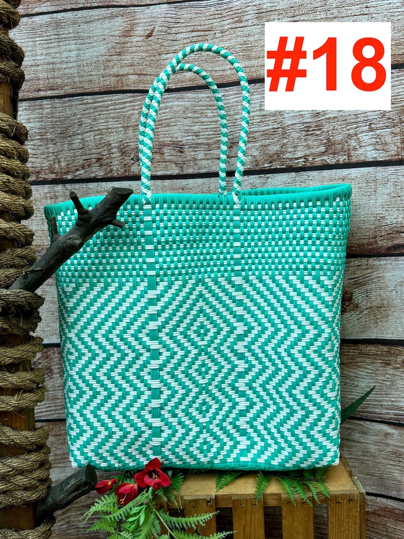 May include: A woven tote bag in turquoise and white, featuring a geometric diamond pattern. The bag has two handles and a rectangular shape. The text "#18" is in the upper right corner. The bag is made of a durable, woven material.