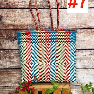 May include: A rectangular tote bag woven from plastic strips in a geometric pattern of red, teal, and metallic gold. The bag features two braided handles in red and gold, and the number #7 is displayed in the upper right corner of the image.