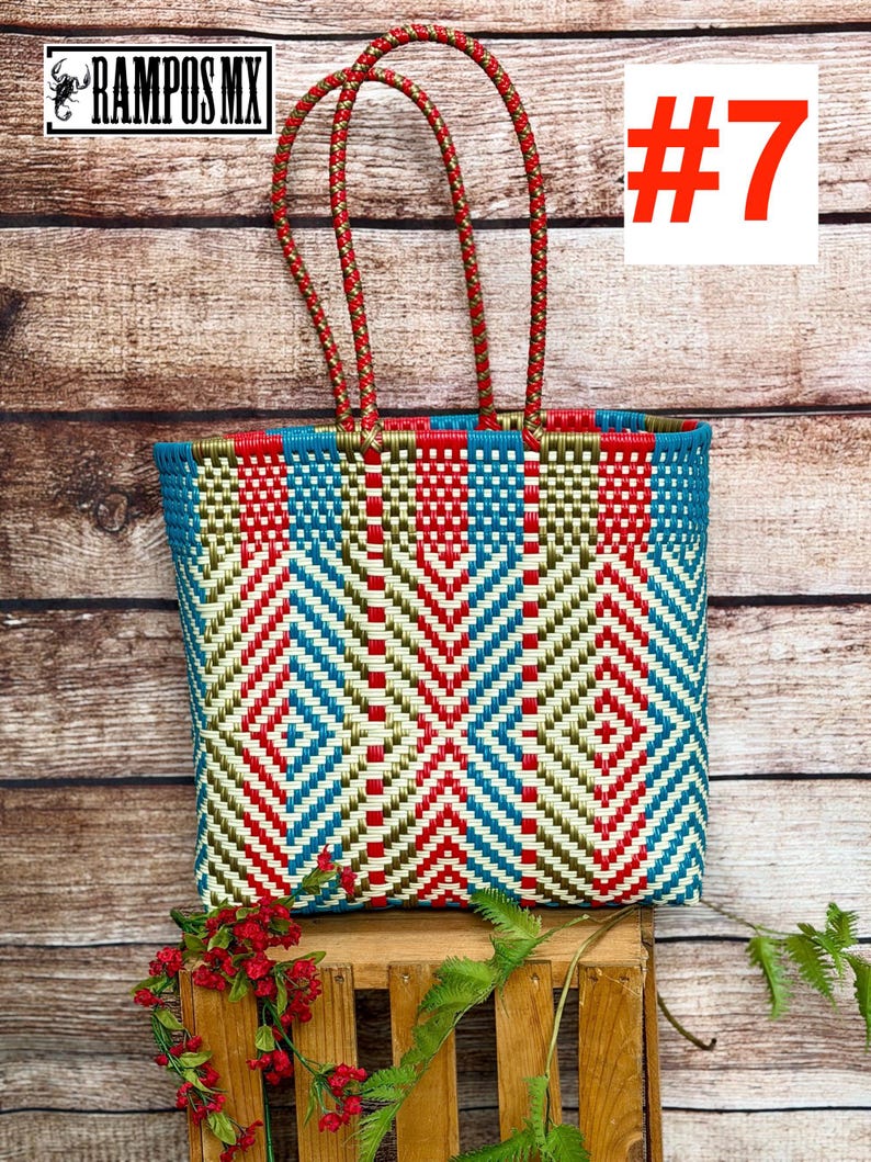 May include: A rectangular tote bag woven from plastic strips in a geometric pattern of red, teal, and metallic gold. The bag features two braided handles in red and gold, and the number #7 is displayed in the upper right corner of the image.