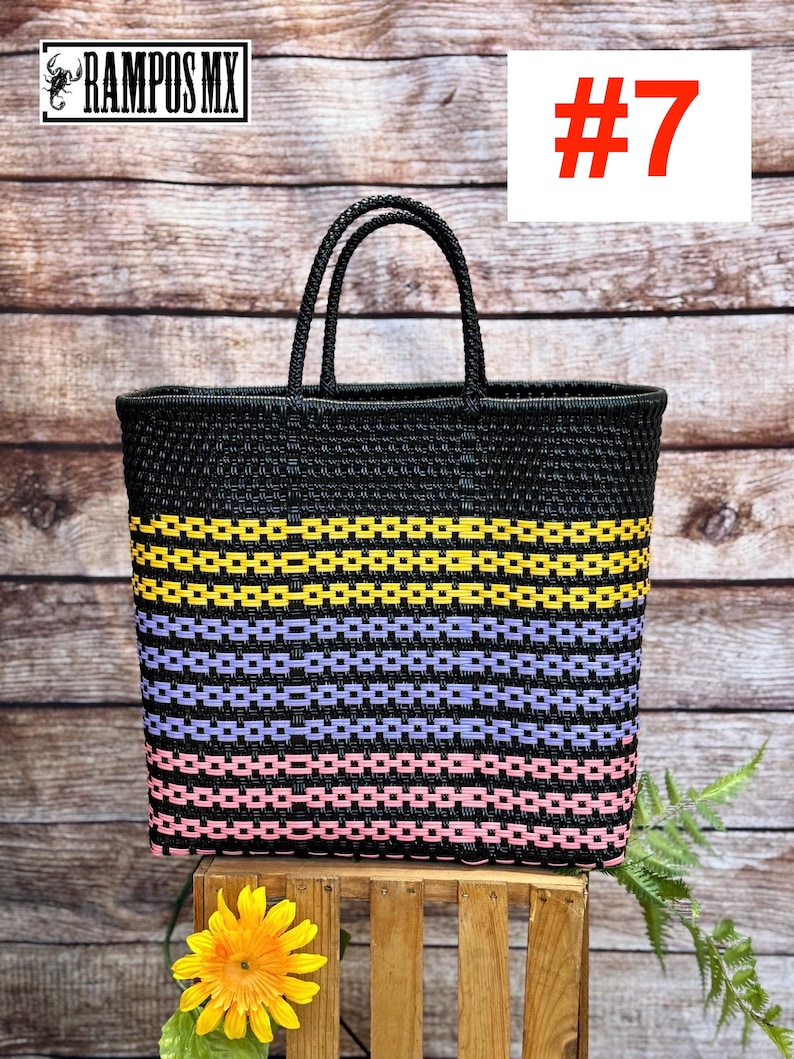 May include: A black woven tote bag with yellow, lavender, and pink horizontal stripes. The bag has two black handles and is displayed on a wooden crate. The number 7 is displayed in red on a white background.
