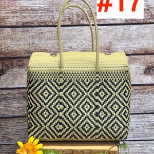 Op de afbeelding: Een rechthoekige draagtas met een geweven patroon van zwarte en beige plastic strips. De tas heeft twee bijpassende beige gevlochten handvatten en een bovenflap die is vastgezet met zilverkleurige metalen knopen. De tekst RAMPOS MX en #17 is zichtbaar.