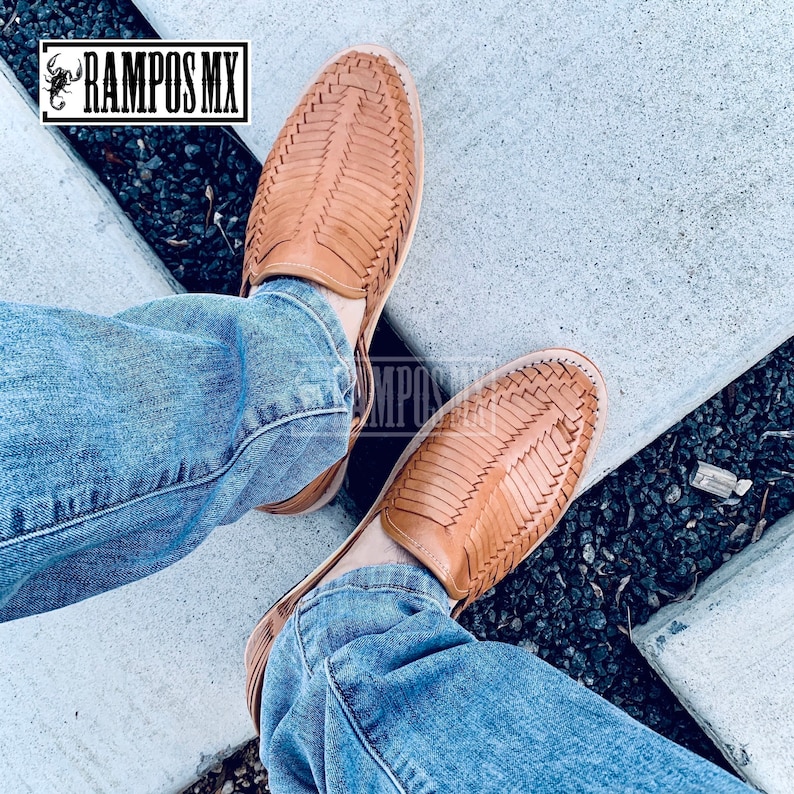 May include: A pair of tan leather sandals with a woven design. The sandals are being worn by someone wearing blue jeans.