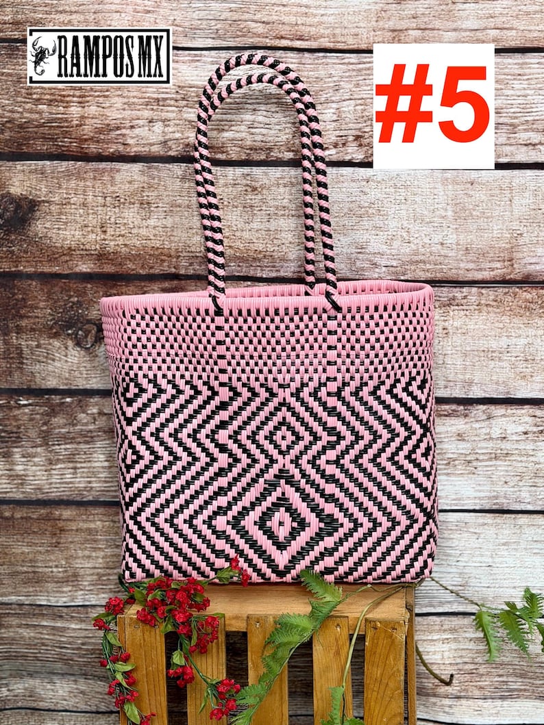 May include: A woven tote bag featuring a geometric diamond pattern in alternating pink and black plastic strips. The bag has two matching pink and black braided handles and displays the text RAMPOS MX and the number #5 in the upper corners.