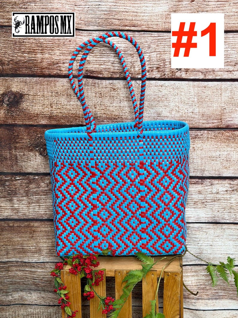 May include: A rectangular tote bag woven from bright blue and red plastic strips in a geometric diamond pattern. The bag features two matching braided blue and red handles attached to the top rim. The text RAMPOS MX and #1 are visible.