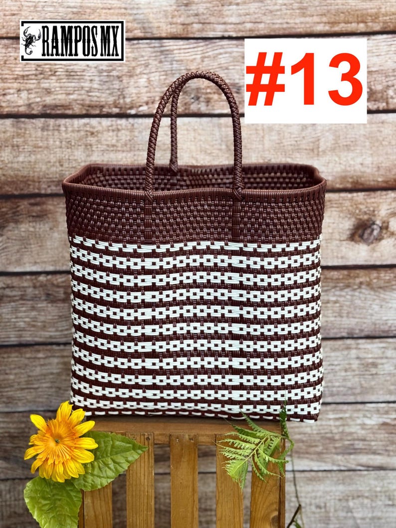 May include: A woven tote bag with a brown top and handles, and a white and brown striped body. The bag has the text "#13" in a red box. The logo "RAMPOS MX" is in the top left corner. A yellow flower and green leaves are in the foreground.