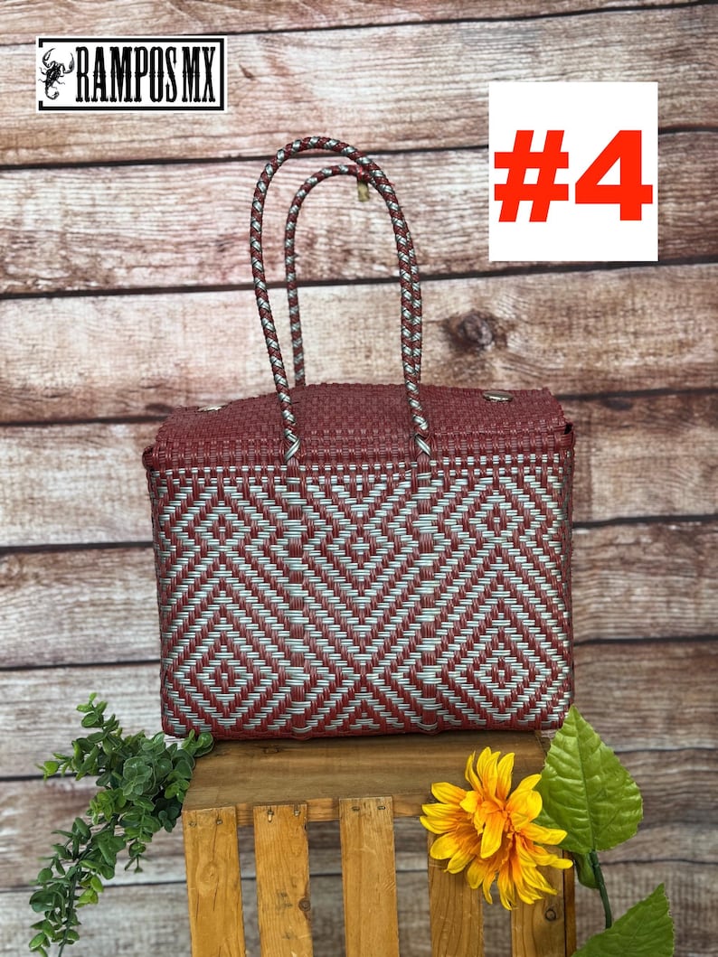 Op de afbeelding: Een rechthoekige gevlochten tas met een geometrisch ruitpatroon in donkerrood en metallic zilver. De tas heeft twee bijpassende gevlochten handvatten en een gestructureerd deksel. De tekst RAMPOS MX en een schorpioen-icoon zijn zichtbaar.