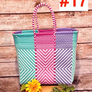 May include: A colorful woven tote bag with a geometric pattern in teal, pink, and purple. The bag has a matching handle and the number 17 in red on a white background. A yellow sunflower and greenery are placed in front of the bag.
