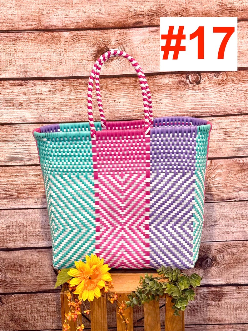 May include: A colorful woven tote bag with a geometric pattern in teal, pink, and purple. The bag has a matching handle and the number 17 in red on a white background. A yellow sunflower and greenery are placed in front of the bag.
