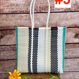 May include: A rectangular tote bag woven from plastic strips in a vertical striped pattern of black, white, and beige, featuring two white braided handles and bright teal side panels. The bag displays the text RAMPOS MX and the number #3.