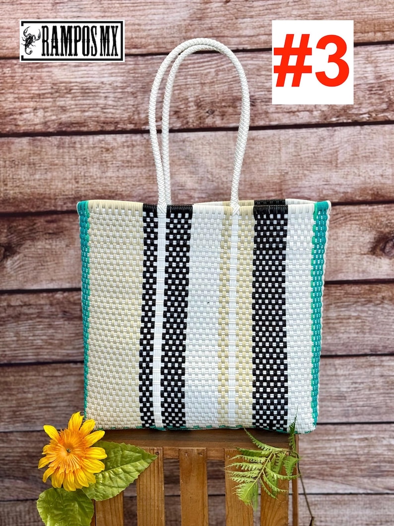 May include: A rectangular tote bag woven from plastic strips in a vertical striped pattern of black, white, and beige, featuring two white braided handles and bright teal side panels. The bag displays the text RAMPOS MX and the number #3.