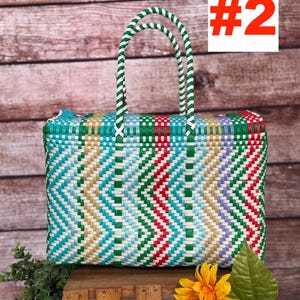 Op de afbeelding: Een rechthoekige geweven plastic tas met een veelkleurig chevronpatroon in groen, rood, lichtblauw, wit en beige. De tas heeft twee gevlochten groen-witte handvatten en bevat de tekst RAMPOS MX en het nummer #2.