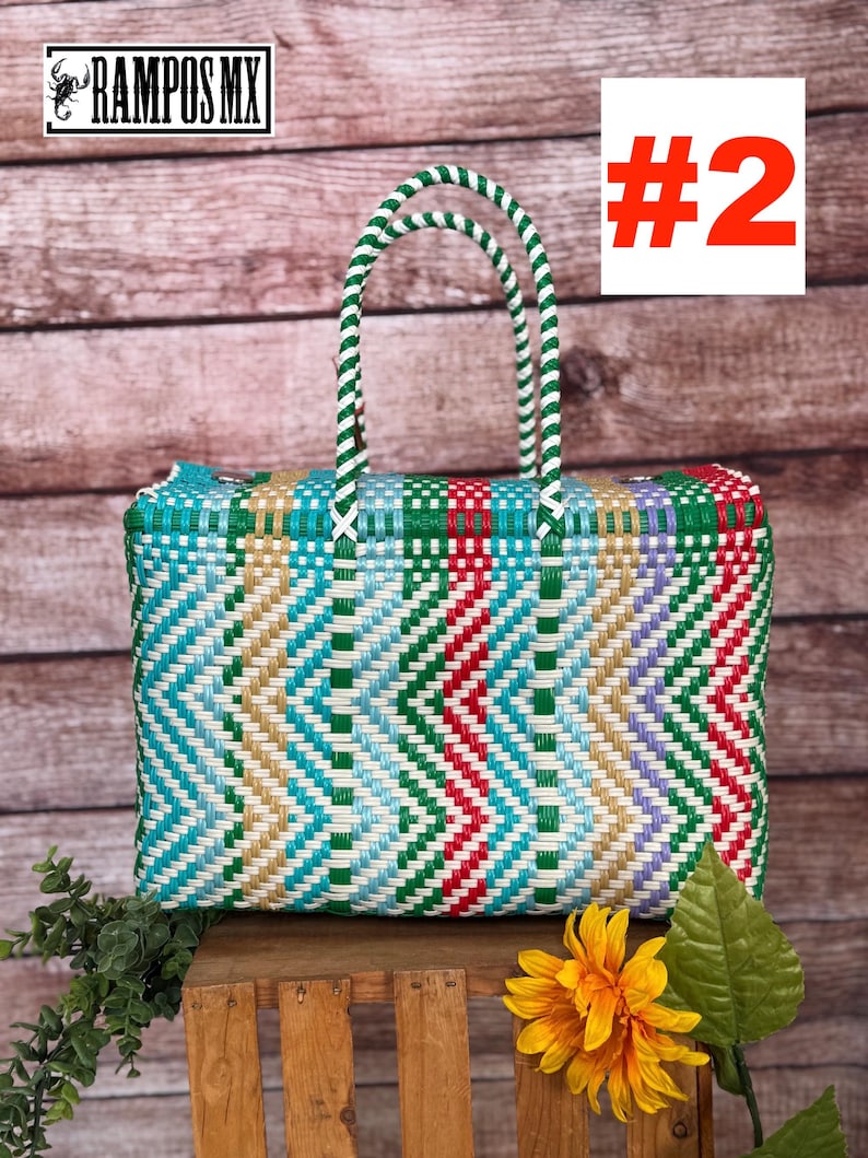 Op de afbeelding: Een rechthoekige geweven plastic tas met een veelkleurig chevronpatroon in groen, rood, lichtblauw, wit en beige. De tas heeft twee gevlochten groen-witte handvatten en bevat de tekst RAMPOS MX en het nummer #2.