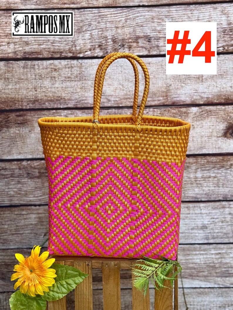 May include: A woven tote bag featuring a gold and hot pink geometric diamond pattern. The bag has two matching gold braided handles and a rectangular structure. The top portion is solid gold, while the lower section displays the diamond design.