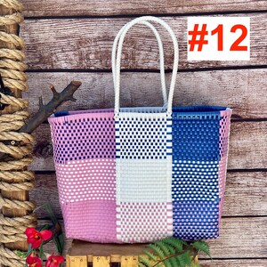 May include: A rectangular woven tote bag featuring a multi-colored grid pattern in shades of pink, white, and blue. The bag has two white woven handles and displays the text #12 in the upper right corner. The construction consists of thin plastic strips.