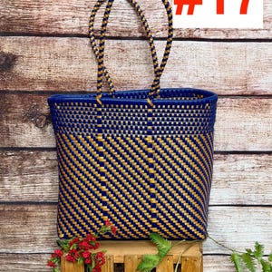 May include: A woven tote bag featuring a diagonal pattern of dark blue and metallic gold plastic strips. The bag has two matching braided handles and a rectangular base. The text RAMPOS MX and the number #17 are visible in the upper corners.
