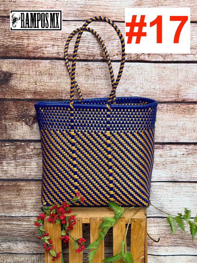 May include: A woven tote bag featuring a diagonal pattern of dark blue and metallic gold plastic strips. The bag has two matching braided handles and a rectangular base. The text RAMPOS MX and the number #17 are visible in the upper corners.