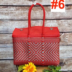 Op de afbeelding: Een rechthoekige mandtas van gevlochten rood en zilverkleurig plastic met twee bijpassende rode gevlochten handvatten. De tas heeft een geometrisch ruitpatroon en twee zilverkleurige metalen sluitingen op het deksel. De tekst RAMPOS MX en #6 is zichtbaar.