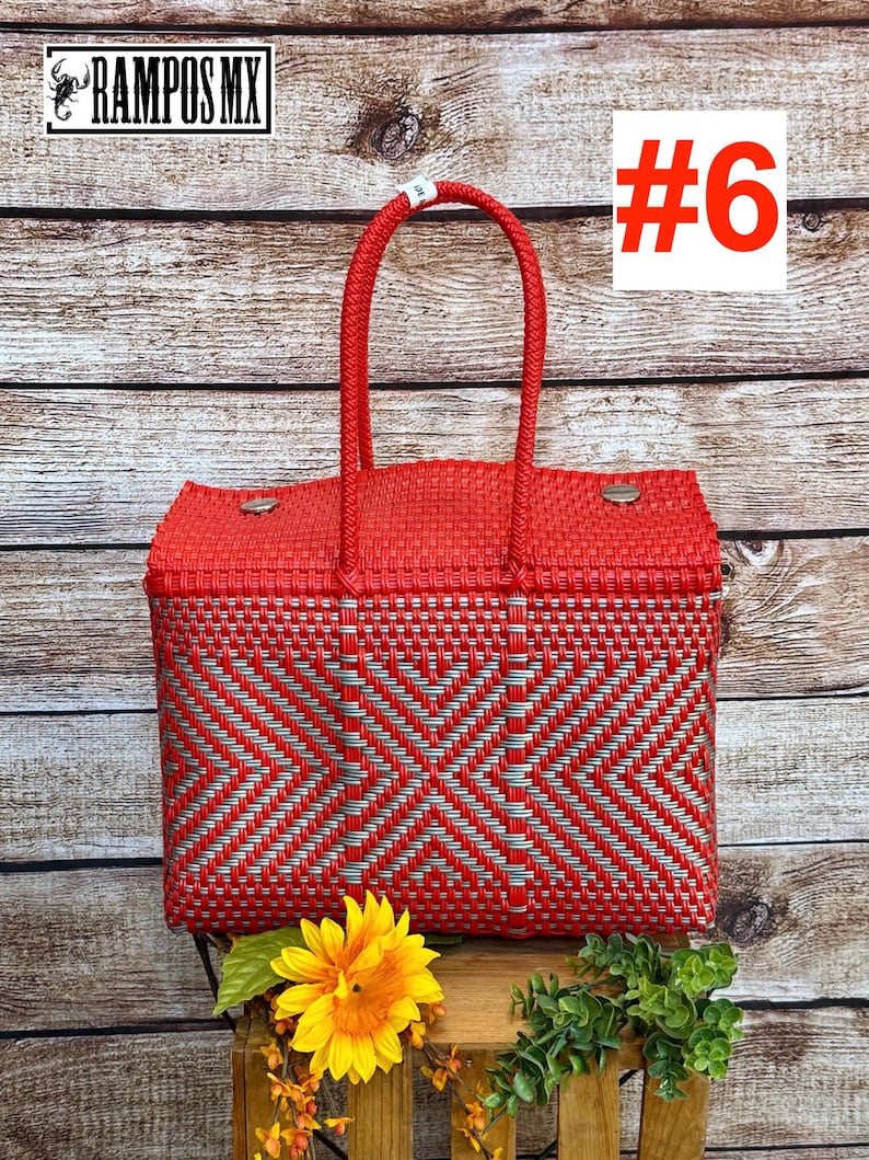 Op de afbeelding: Een rechthoekige mandtas van gevlochten rood en zilverkleurig plastic met twee bijpassende rode gevlochten handvatten. De tas heeft een geometrisch ruitpatroon en twee zilverkleurige metalen sluitingen op het deksel. De tekst RAMPOS MX en #6 is zichtbaar.