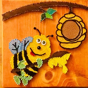 May include: A yellow and black bee with blue wings and big eyes is perched on a brown branch with green leaves. The bee is smiling and has a red tongue sticking out. A yellow honeycomb is in the background.