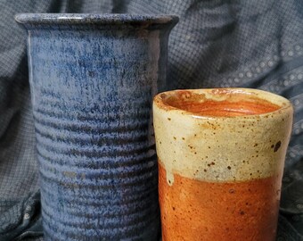 Könnte beinhalten: Zwei Keramikvasen, eine blaue und eine mit brauner und beiger Glasur. Die blaue Vase hat ein gestreiftes Muster. Eine kleine orangefarbene bemalte Schildkrötenfigur befindet sich im Vordergrund.