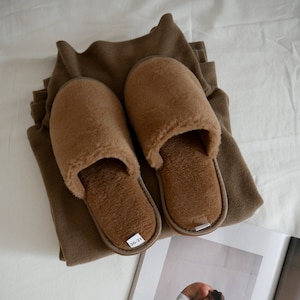 May include: A pair of brown fuzzy slippers with a size tag that reads "36-37". The slippers are on top of a folded brown sweater.
