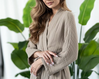 May include: A woman wearing a light brown waffle-weave robe with long sleeves and a tie belt. The robe is made of a soft, comfortable fabric and has a relaxed fit.