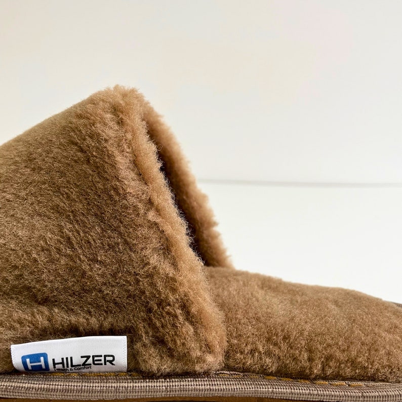 May include: Close-up of a brown faux fur slipper with a brown leather sole and a Hilzer brand label. The slipper is made of soft, plush material.