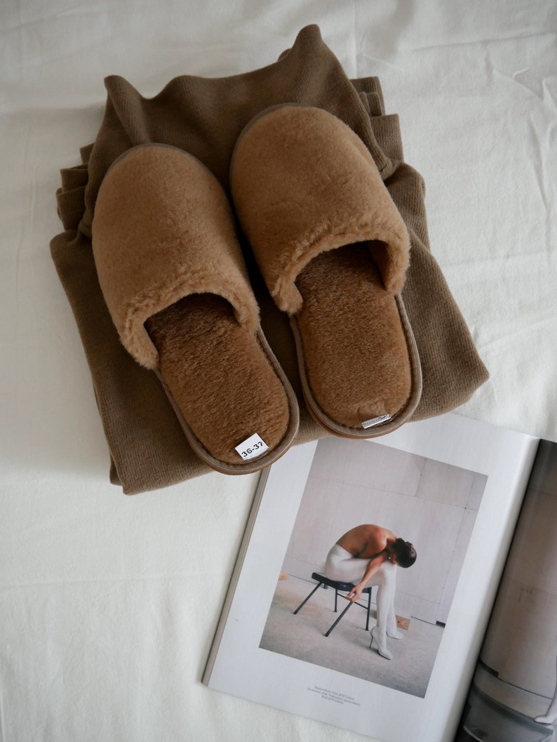 May include: A pair of brown fuzzy slippers with a size tag that reads "36-37". The slippers are on top of a folded brown sweater.