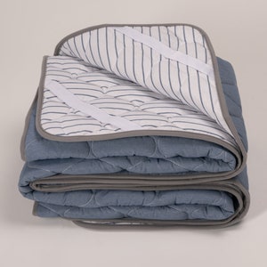 May include: A folded blue and gray quilted mattress pad with white stripes and elastic straps.