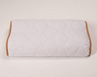 May include: A white pillow with a quilted pattern and a brown trim. The pillow is on a white background.