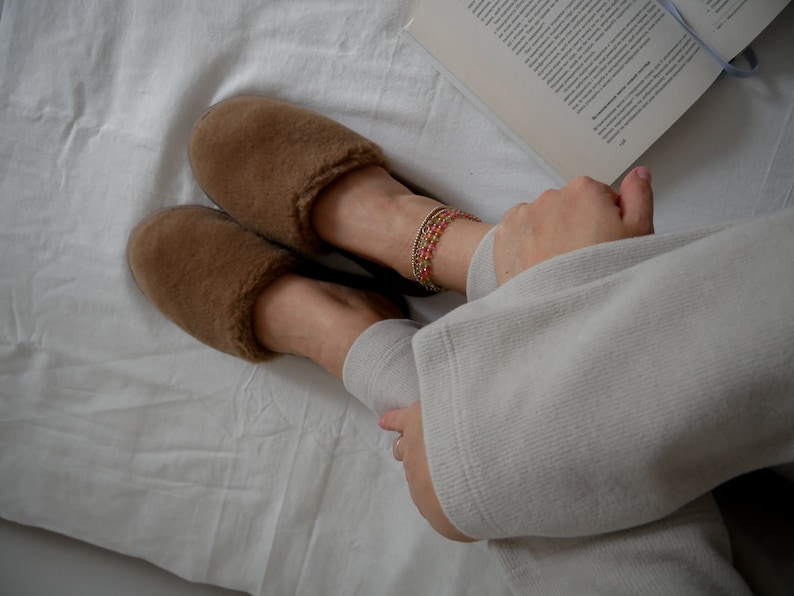 May include: A pair of brown fuzzy slippers with a white background. The slippers are worn by a person wearing a white sweater.