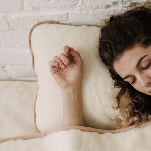 Puede incluir: Primer plano de una persona durmiendo sobre una almohada blanca con una funda de almohada de color crema. La mano de la persona está apoyada en la almohada y su cabello cubre parte de la almohada.