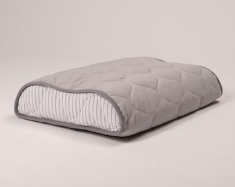 May include: A grey and white quilted pillow with a curved shape. The pillow has a striped pattern on one side and a quilted pattern on the other side.