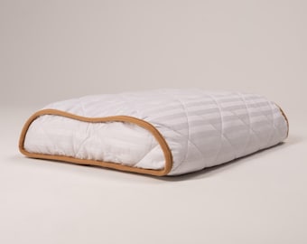 May include: A white and grey striped pillow with a brown quilted border. The pillow is designed for sleeping and has a curved shape.