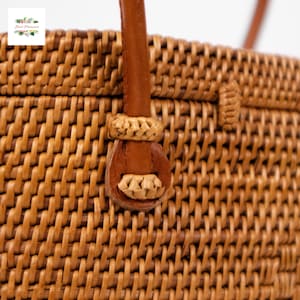 Puede incluir: Primer plano de un bolso de mano de rat&aacute;n tejido con asa y detalles en cuero marr&oacute;n. El bolso presenta un patr&oacute;n tejido apretado en color marr&oacute;n natural. El asa est&aacute; sujeta con detalles decorativos tejidos.