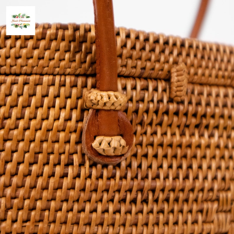 Puede incluir: Primer plano de un bolso de mano de rat&aacute;n tejido con asa y detalles en cuero marr&oacute;n. El bolso presenta un patr&oacute;n tejido apretado en color marr&oacute;n natural. El asa est&aacute; sujeta con detalles decorativos tejidos.