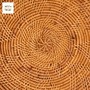 Op de afbeelding: Close-up van een geweven rotan mand met een spiraalvormig ontwerp. Het natuurlijke bruine materiaal is strak geweven in concentrische cirkels, waardoor een textuur ontstaat. Het midden heeft een klein, stervormig detail. De mand is waarschijnlijk handgemaakt.