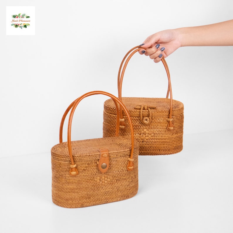 Puede incluir: Dos bolsos ovalados de rat&aacute;n tejido con asas y cierres de cuero marr&oacute;n. Los bolsos son de color marr&oacute;n claro natural y tienen una forma cl&aacute;sica y estructurada. Una persona sostiene un bolso.