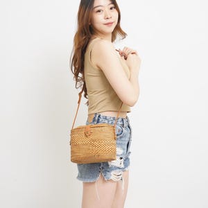 Peut inclure: Un sac &agrave; bandouli&egrave;re rectangulaire en rotin tress&eacute; avec une bandouli&egrave;re en cuir marron et une fermeture &agrave; bouton. Le sac est de couleur marron clair naturel. Le sac est port&eacute; en bandouli&egrave;re.