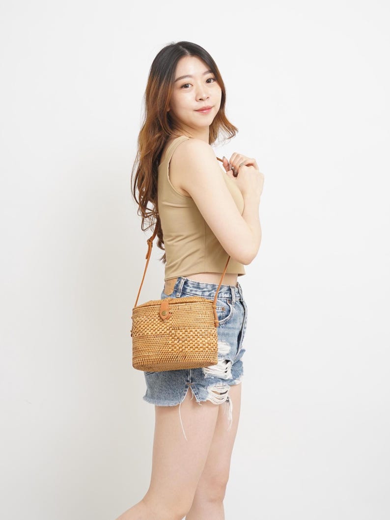Peut inclure: Un sac &agrave; bandouli&egrave;re rectangulaire en rotin tress&eacute; avec une bandouli&egrave;re en cuir marron et une fermeture &agrave; bouton. Le sac est de couleur marron clair naturel. Le sac est port&eacute; en bandouli&egrave;re.
