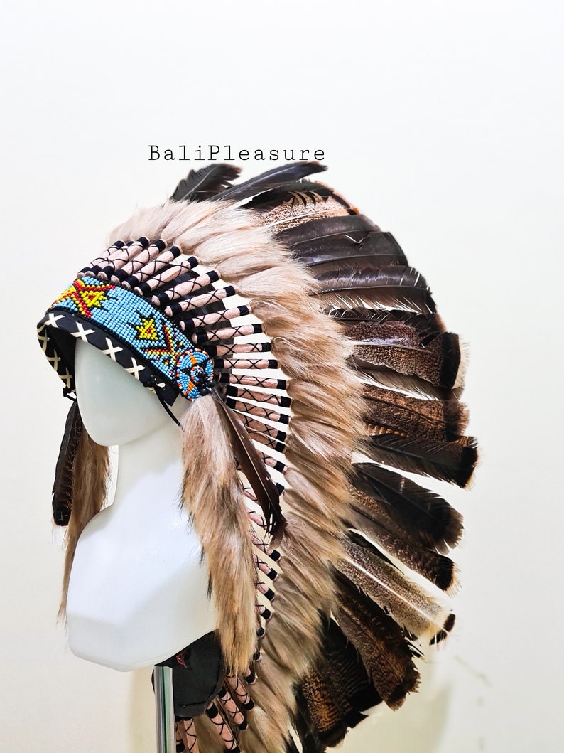 May include: A Native American headdress with a black, blue, and yellow beaded headband. The headdress features brown and black feathers, and tan fur trim. The text "BaliPleasure" is visible.