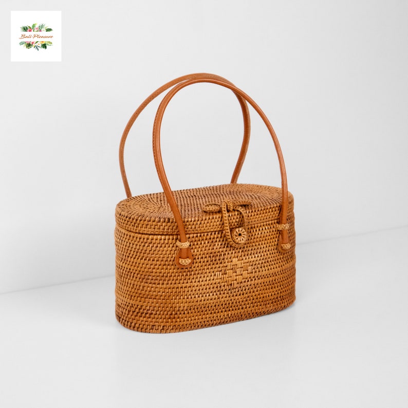 Puede incluir: Bolso de mano ovalado de rat&aacute;n con dise&ntilde;o tejido y asas de cuero marr&oacute;n. El bolso tiene un cierre de broche y es de color marr&oacute;n claro. Las asas son curvas y est&aacute;n unidas a la parte superior.