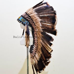 May include: A Native American headdress with brown and black feathers, displayed on a mannequin head. The headdress features a beaded band with blue, yellow, and black accents. The text "BaliPleasure" is visible on the image.