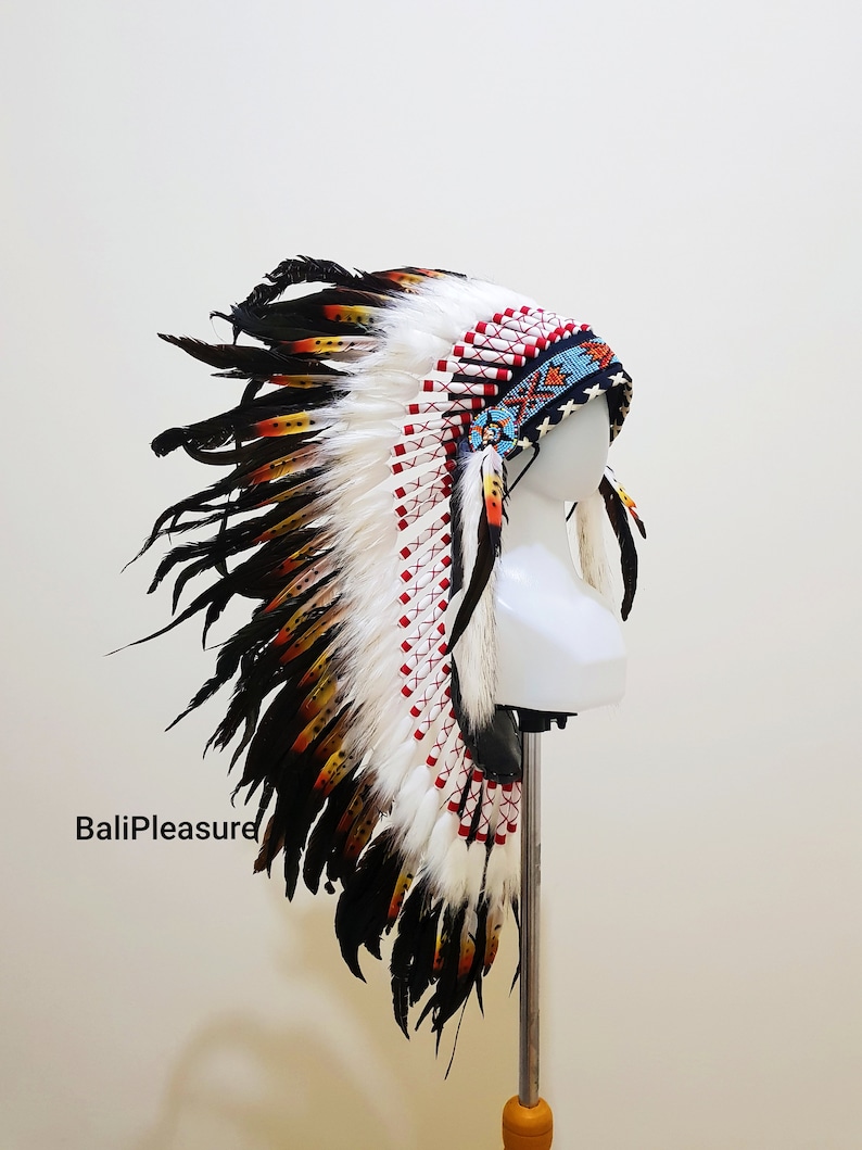 May include: A Native American headdress with white, black, orange, and yellow feathers. The headdress has a beaded headband with red and blue accents. The feathers are arranged in a fan shape, with the longest feathers at the back.