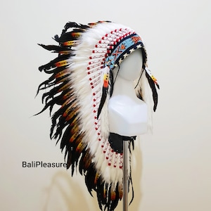 Op de afbeelding: Een Indiaanse hoofdtooi met witte, zwarte, gele en rode veren. De hoofdband is voorzien van kralen in blauw, rood en oranje. De tekst "BaliPleasure" is zichtbaar aan de linkerkant van de afbeelding.