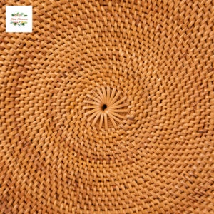 May include: Close-up of a woven rattan object with a spiral pattern. The natural-toned material is tightly woven in a circular design, with a central hole. The texture is visible, and the overall appearance is rustic and handcrafted.