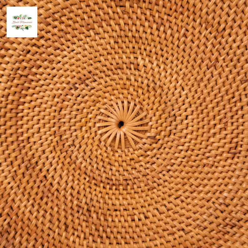 May include: Close-up of a woven rattan object with a spiral pattern. The natural-toned material is tightly woven in a circular design, with a central hole. The texture is visible, and the overall appearance is rustic and handcrafted.