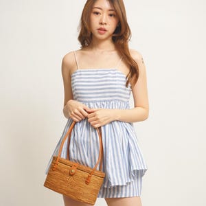 Puede incluir: Conjunto de dos piezas a rayas azules y blancas, con un bolso de mano tejido a juego. El conjunto incluye un top con tirantes finos y un pantal&oacute;n corto. El bolso tiene asas de cuero marr&oacute;n y un cierre.